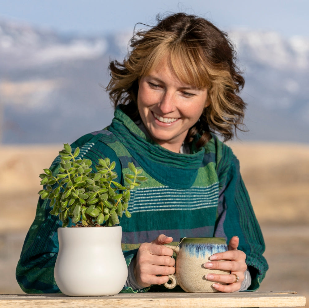 Woman with tea looking at bear claw succulent houseplant plant pot