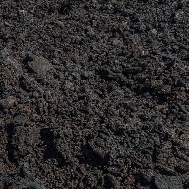 A detailed close-up of dark, textured volcanic soil and rocks, showcasing its rugged and nutrient-rich composition.