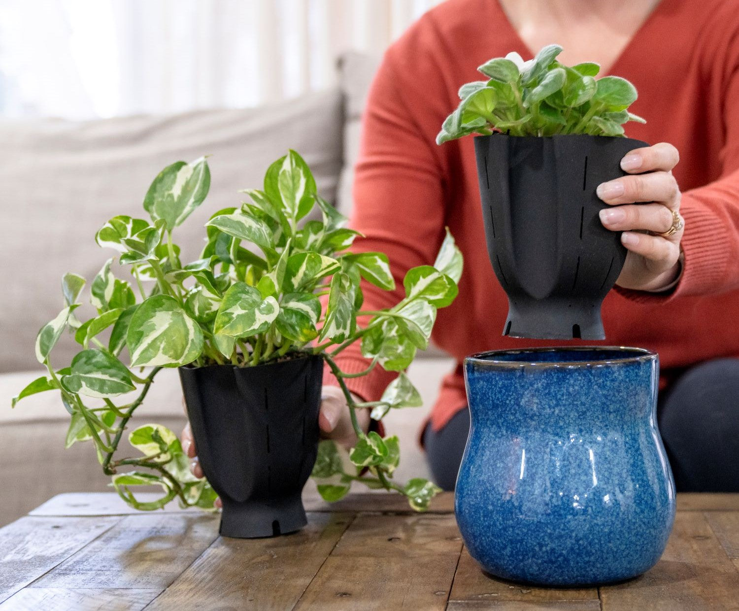 Hands demonstrating the use of Happy Roots flexible liners, placing plants into a blue ceramic pot on a wooden table.