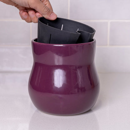 Hand lifting liner out of curvy purple violet Happy Roots Plant Pot